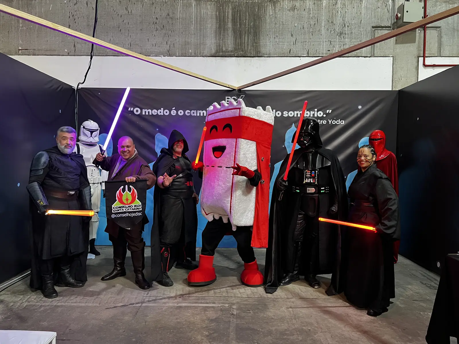 Grupo de cosplayers de Star Wars com sabres de luz posando ao lado do mascote Ticão