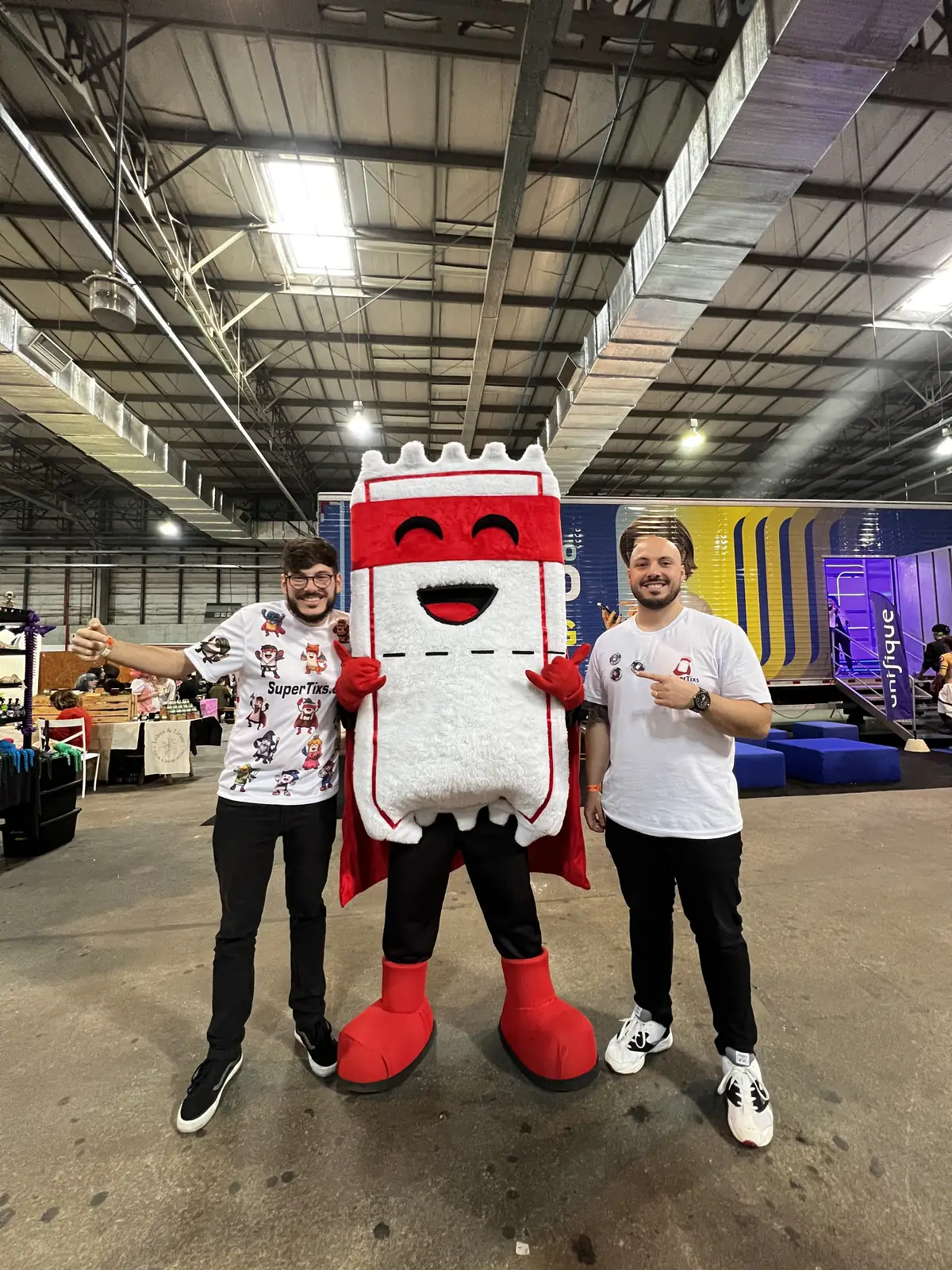 O mascote Ticão entre dois integrantes da equipe SuperTixs no pavilhão de uma convenção