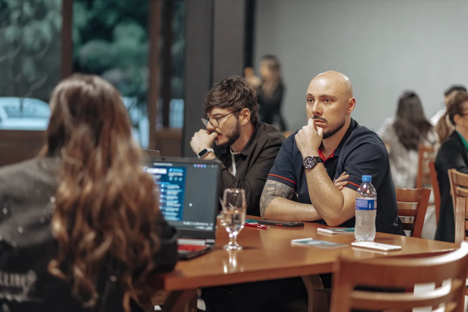 Participantes em uma mesa de workshop com notebook aberto, atentos à apresentação